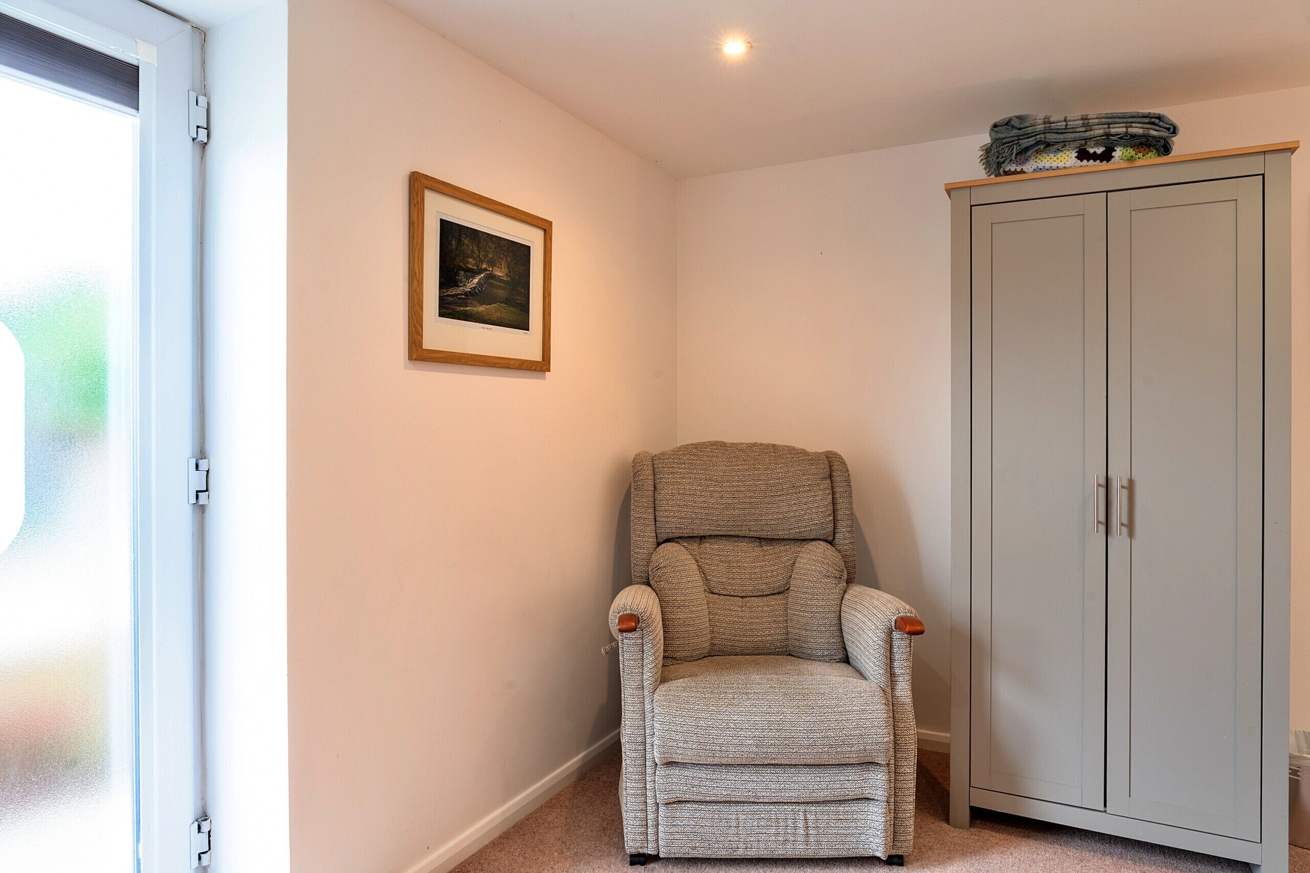 A corner room with a grey armchair, a wardrobe, and a framed picture on the wall.