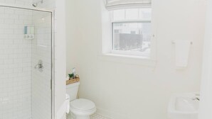 A bathroom with a glass shower enclosure, a toilet, a sink, and a window.
