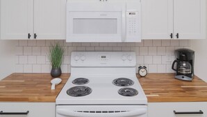 A kitchen with white cabinets, a white microwave, a stove, a coffee maker, and a clock.