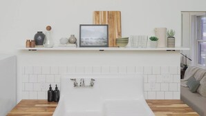 A modern bathroom with a freestanding bathtub, white tiled walls, and a wooden floor.