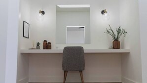 A minimalist bathroom with a wooden floor, a white vanity with a mirror, two wall-mounted lights, and a potted plant. - Room 2-3 (Tulsa)