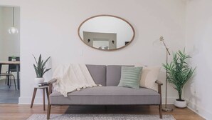 A living room with a grey sofa, a round mirror, a potted plant, and a small table. - Room 2-4 Summary:<br>In (Tulsa)