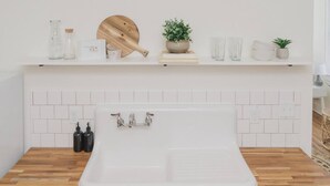 Eine moderne Küche mit einem großen, weißen Spülbecken, einer Holz Arbeitsplatte und einer weißen, gefliesten Rückwand.