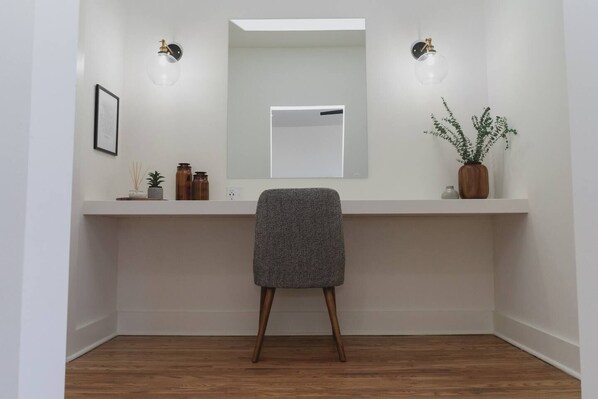 A minimalist bathroom with a wooden floor, a grey chair, a white vanity with a mirror, and two wall-mounted lights.