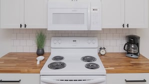 A kitchen with white cabinets, a white microwave, a stove, a coffee maker, and a clock. - Room 3-3 (Tulsa)