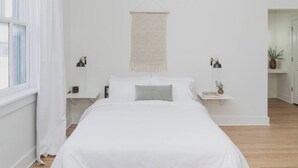 A minimalist bedroom with a large bed, bedside tables with lamps, a macrame wall hanging, and a view of a hallway. - Room 3-3 (Tulsa)