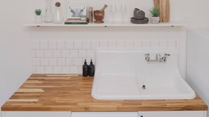 A kitchen with a wooden countertop, white cabinets, a white sink, and a white tiled backsplash. - Room 3-3 (Tulsa)