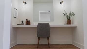 A modern bathroom with a white vanity, a mirror, two wall-mounted lights, a framed picture, and a potted plant.