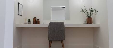 A modern bathroom with a white vanity, a mirror, two wall-mounted lights, a framed picture, and a potted plant.