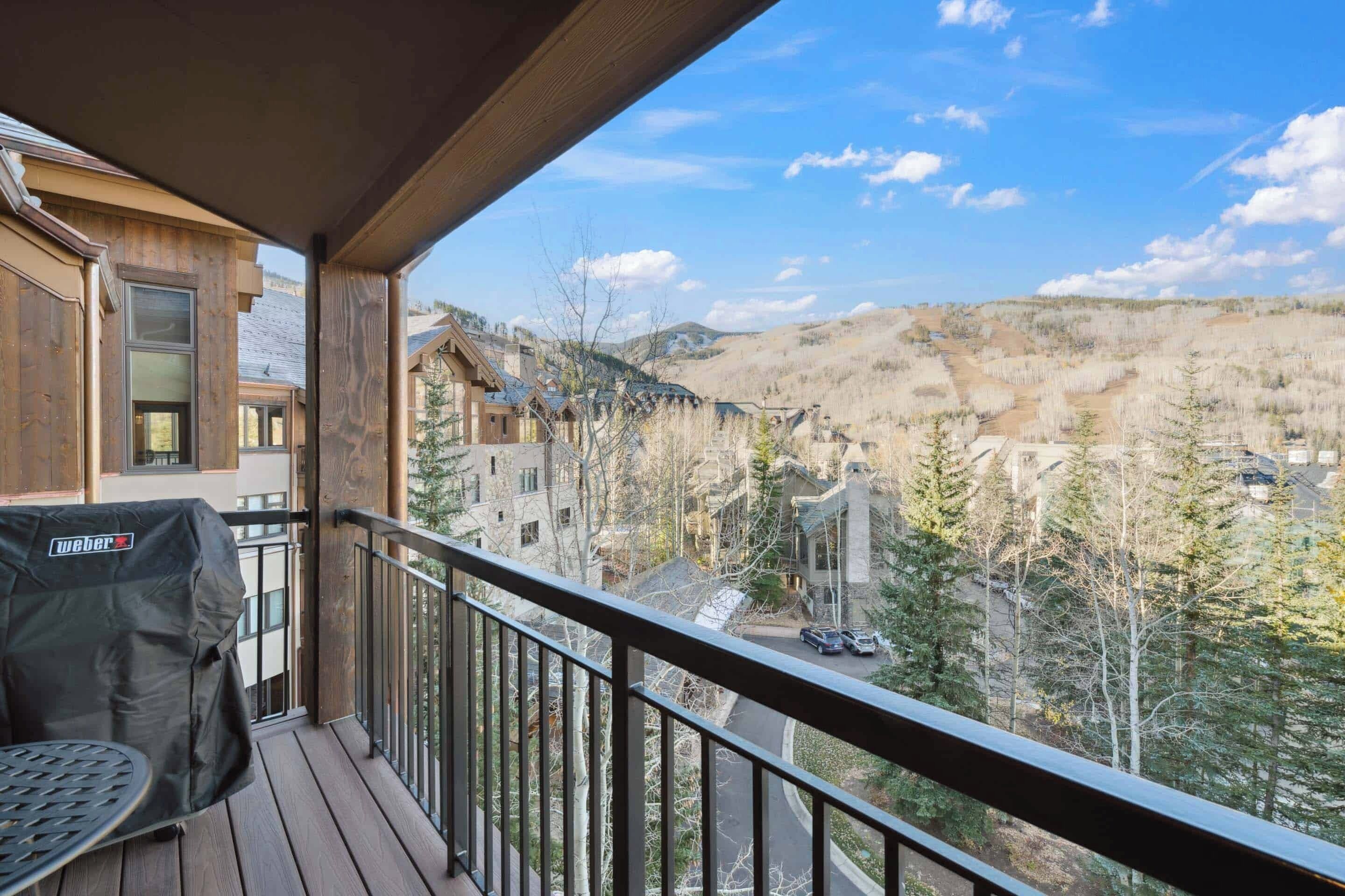 A wooden deck with a grill, overlooking a residential area with houses and trees.