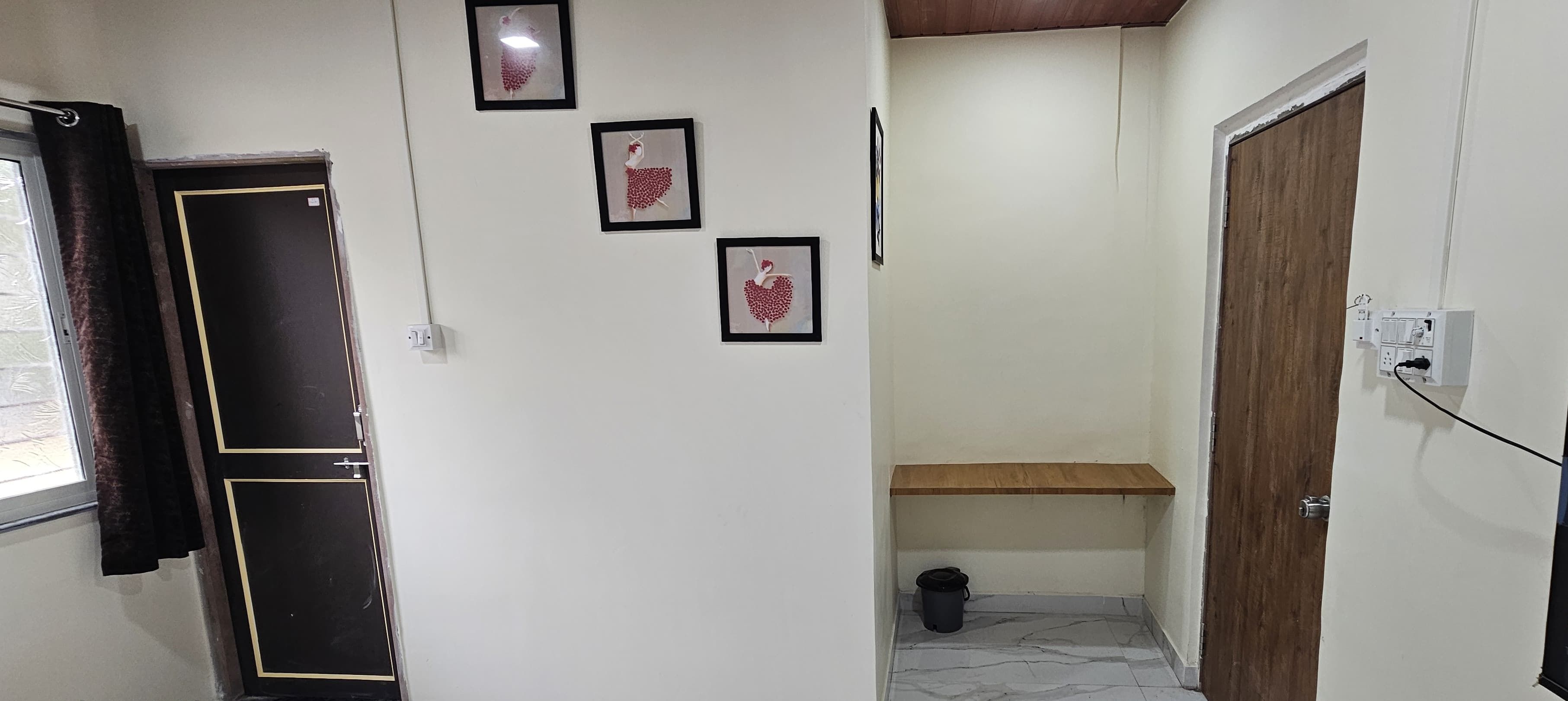 A hallway with a black door, a window with a curtain, and three framed pictures on the wall.