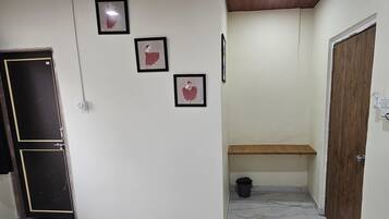A hallway with a black door, a window with a curtain, and three framed pictures on the wall.