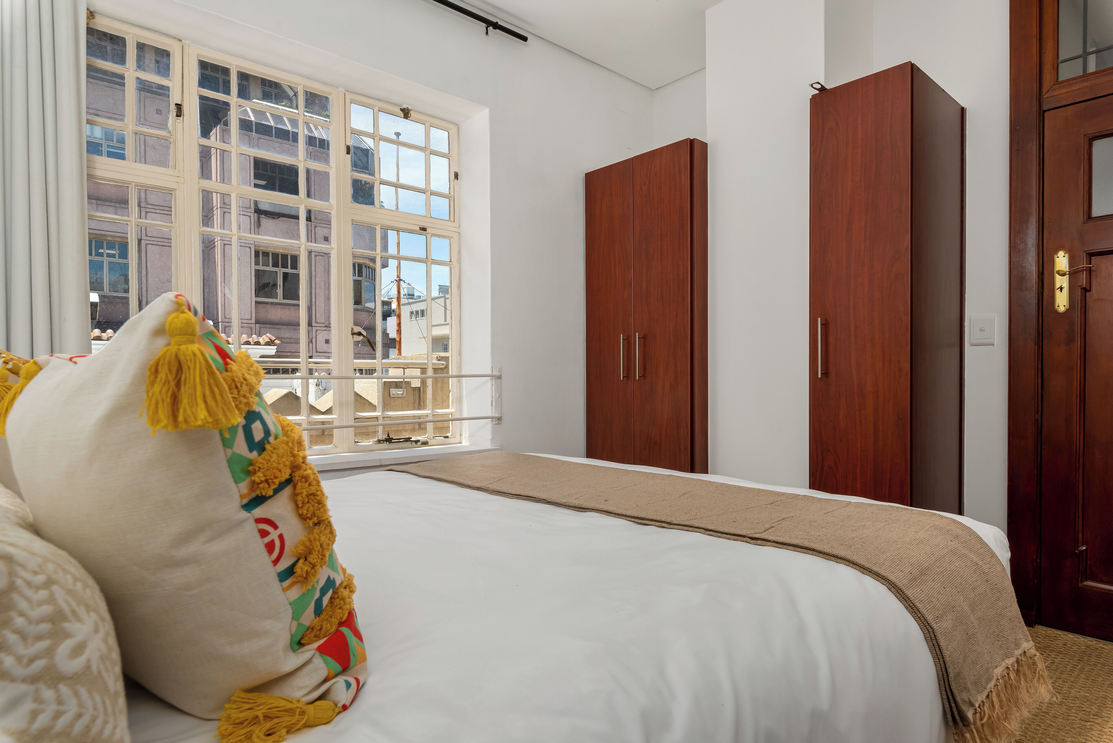 A bedroom with a large bed, a window with a view, and two wooden wardrobes.