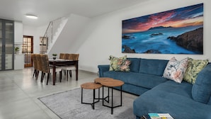 A modern living room with a blue sofa, a dining table with chairs, and a staircase.