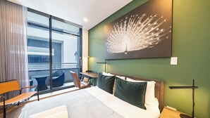 Une chambre d’hôtel avec un grand lit, un bureau, une chaise, une vue sur l’extérieur et une œuvre d’art représentant un paon accrochée au mur.