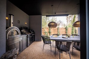 An outdoor kitchen with a grill, a built-in oven, and a dining table with chairs. - Studio Brondesbury - Communal Gym, Gardens, Cinema (London)