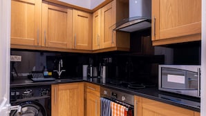 A compact kitchen with wooden cabinets, a built-in oven, a microwave, and a washing machine. - The Courtfield - Studio Lower Ground in Kensington (London)
