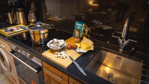 A kitchen with a stainless steel sink, a cutting board with mushrooms, a knife, a pot, a wine glass, and a coffee maker.