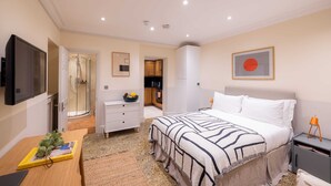 A bedroom with a bed, bedside table, TV, and a bathroom with a shower.