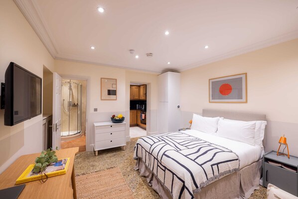 A bedroom with a bed, bedside table, TV, and a bathroom with a shower. - The Courtfield - Studio Lower Ground in Kensington (London)