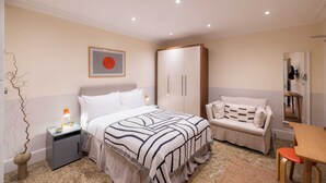 A bedroom with a bed, nightstand, bedside lamp, wardrobe, sofa, and a small table. - The Courtfield - Studio Lower Ground in Kensington (London)