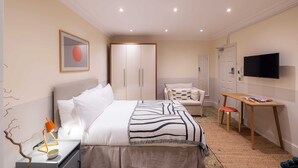 A modern bedroom with a bed, bedside table, TV, wardrobe, and a desk with a chair. - The Courtfield - Studio Lower Ground in Kensington (London)