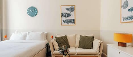 Une chambre d’hôtel avec un lit, un canapé, une table basse avec un livre, une lampe et des œuvres d’art murales.