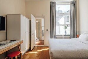 Habitació d'hotel amb llit, escriptori, cadira, armari i finestra amb cortines.