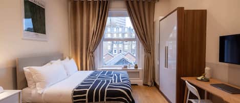 A hotel room with a bed, a desk, a chair, a TV, and a window with curtains.