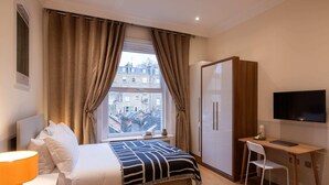 A hotel room with a bed, a desk, a chair, a TV, and a wardrobe. - The Courtfield - Studio Apartment in Kensington (London)