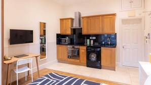 A compact kitchen with wooden cabinets, a microwave, oven, and a washing machine. - The Courtfield - Studio Apartment in Kensington (London)