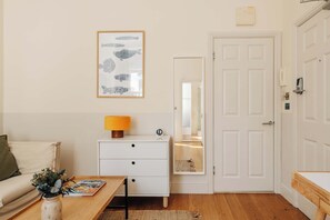 A room with a white door, a framed fish illustration on the wall, a white dresser with drawers, a wooden table with a lamp, and a magazine.