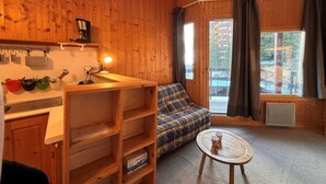 Ein gemütliches Blockhauszimmer mit Holzwänden, einer Küchenzeile, einem karoüberzogenen Sofa und einem kleinen runden Tisch.