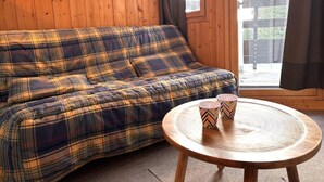 Ein Zimmer mit einem Karosobsofa, einem runden Holztisch mit zwei gemusterten Tassen und einem Fenster mit Vorhängen.