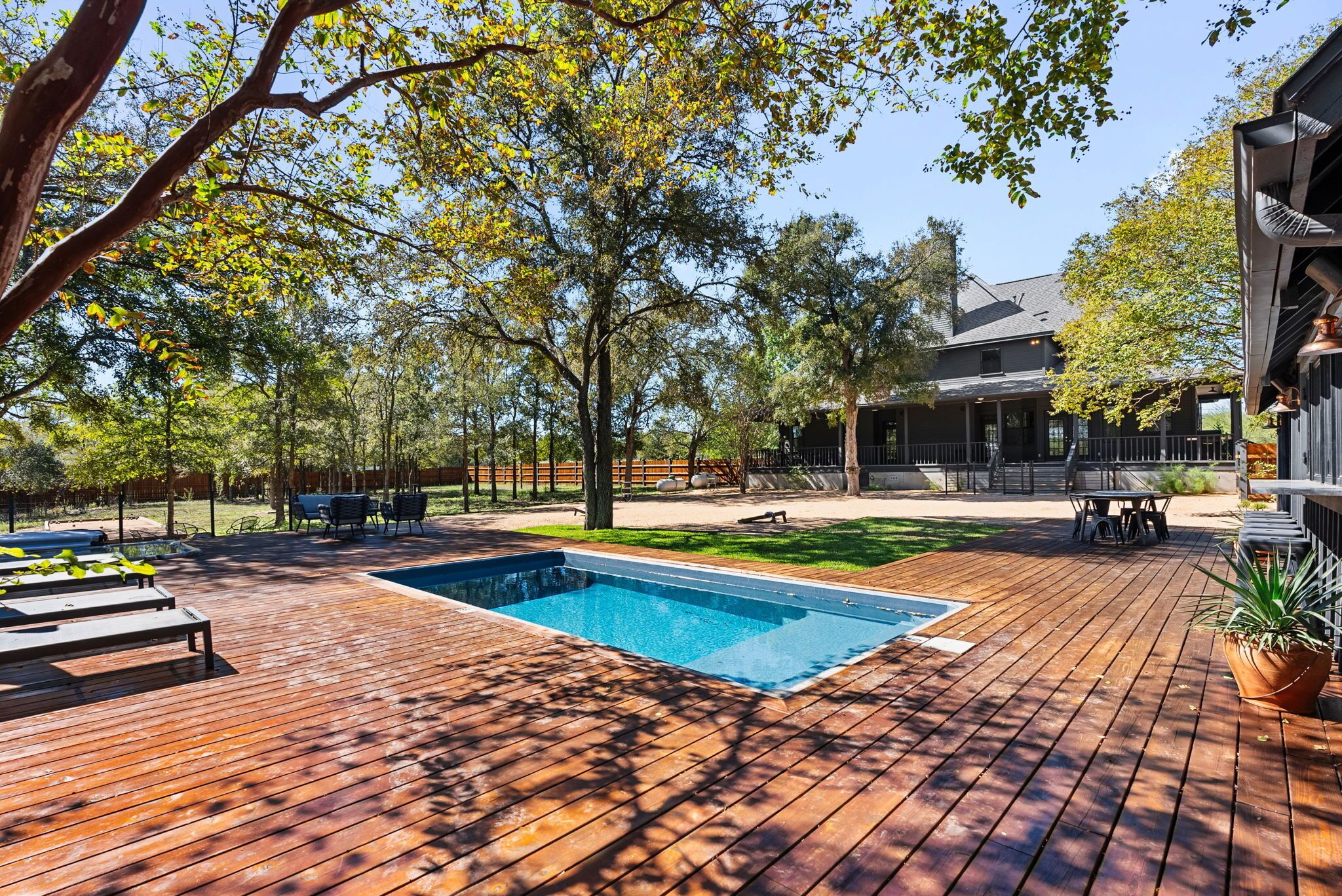 A wooden deck with a swimming pool, outdoor furniture, and a covered patio area.