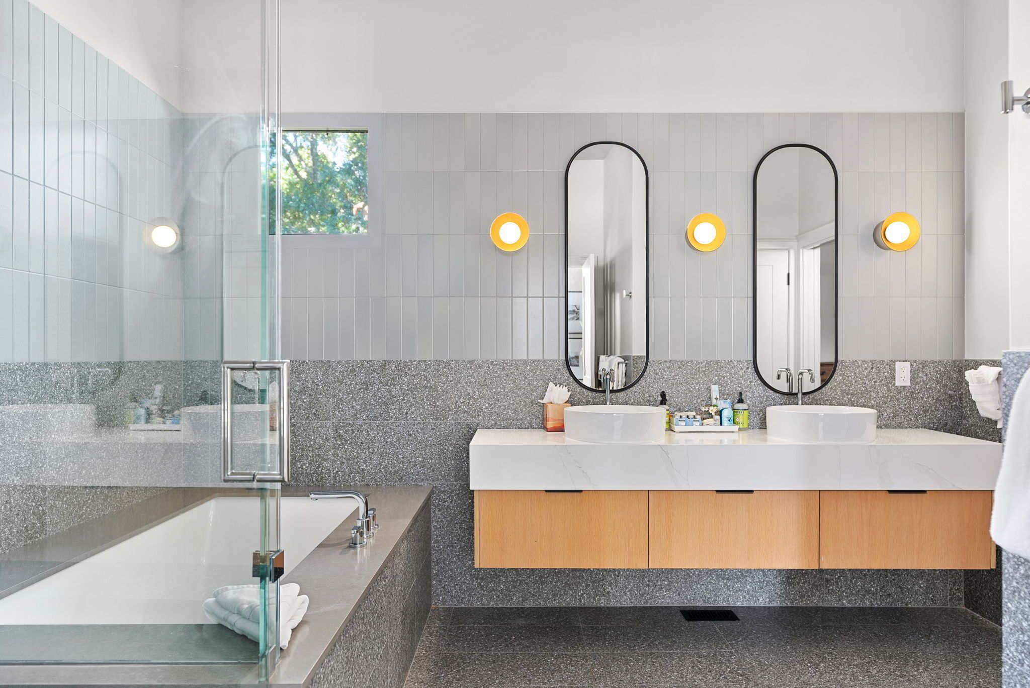 A modern bathroom with a glass shower enclosure, two sinks with mirrors, and a vanity with a marble countertop.