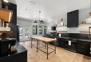A modern kitchen with black cabinetry, a wooden table, and pendant lighting.