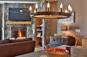 Een woonkamer met een stenen openhaard, een flatscreen televisie, een houten salontafel en een moderne kroonluchter.
