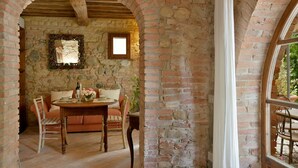 Une pièce rustique aux murs en briques apparentes, une table en bois dressée pour le repas, un banc rembourré et une petite fenêtre.