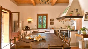 Un grand espace à manger avec une table et des chaises en bois, une cuisine équipée d’une cuisinière et d’un four, et une grande fenêtre donnant sur un paysage verdoyant.