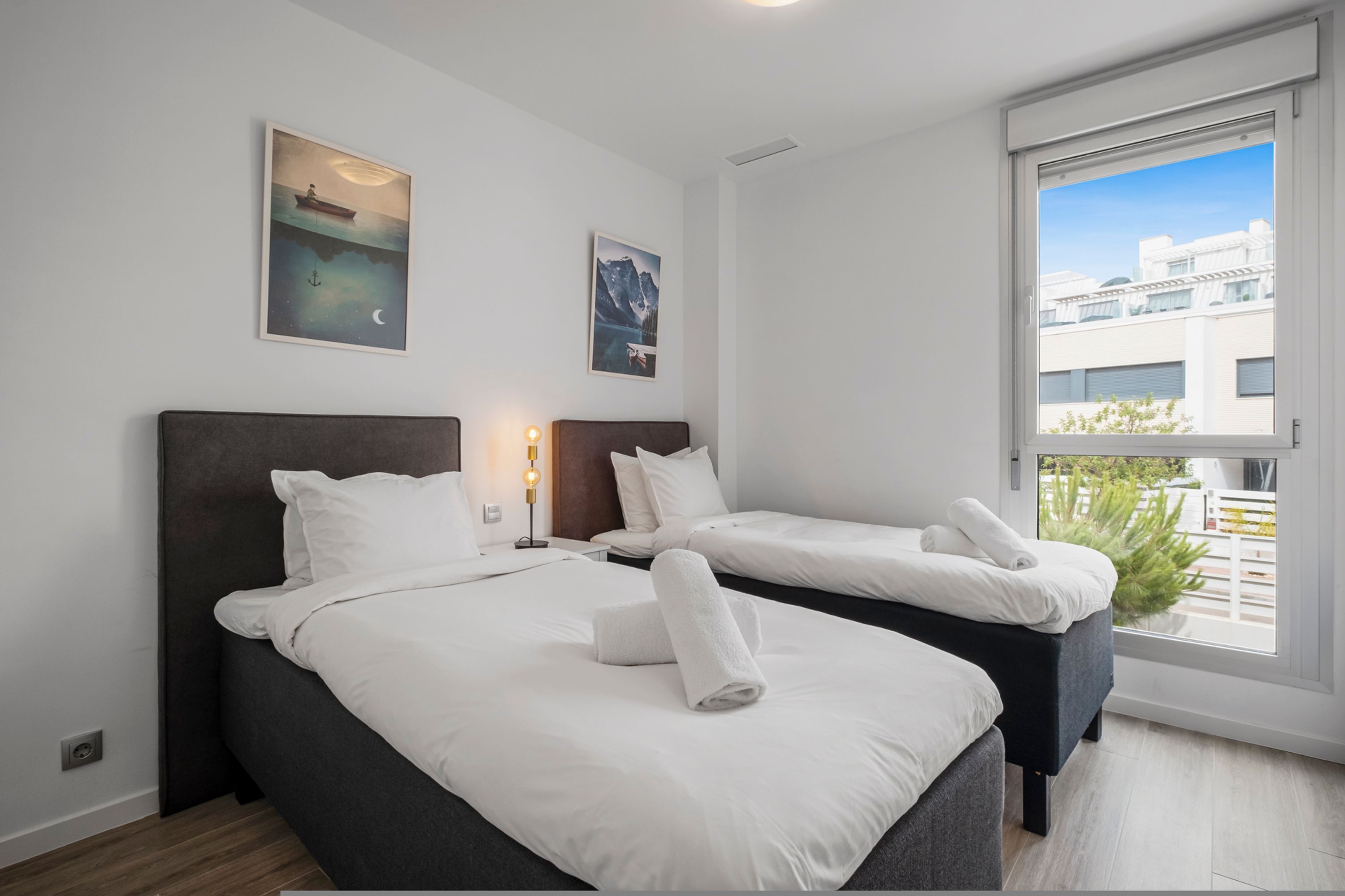 Une chambre d’hôtel avec deux lits, une grande fenêtre donnant sur des immeubles et des œuvres d’art accrochées aux murs.
