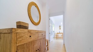 Eine Holzkabine mit Schubladen und einem Korbwägelchen, ein gewobener Spiegel an der Wand und ein Blick in einen Essbereich mit Stühlen und einem Tisch.