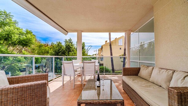 Ein Balkon mit Korbmöbeln, einem Glastisch und einer Couch.