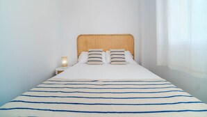 Ein ordentlich gemachtes Bett mit gestreifter Decke, einer Nachttischlampe und einem hölzernen Kopfteil.
