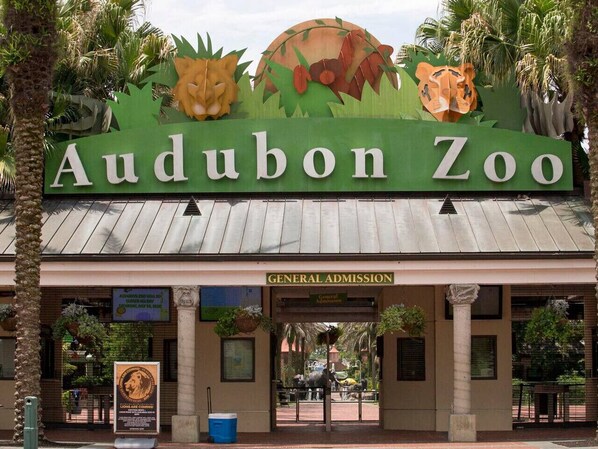 The entrance to Audubon Zoo with a sign for general admission and a decorative archway featuring animal motifs.