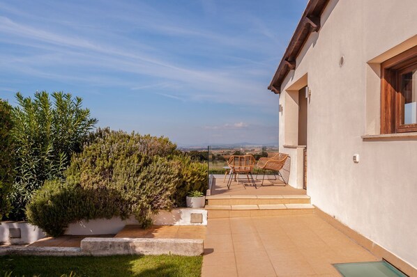 A modern house with a patio, two wicker chairs, and a view of the countryside.