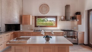 Eine moderne Küche mit Holzschränken, einer Mittelinsel, einem eingebauten Herd und einem Fenster mit Blick auf einen Garten.