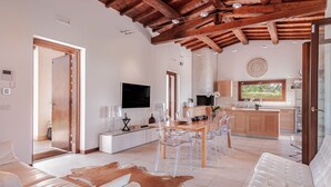 Ein modernes Wohnzimmer mit Holzbalkendecke, einem Essbereich mit klaren Stühlen, einer Küche mit Holzausstattung und einem großen Fenster.
