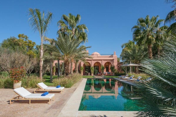A poolside area with lounge chairs, a clear pool, and a building with arches in the background.