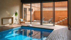 A modern indoor pool area with a clear view of the pool, lounge chairs, and a staircase leading to an upper level.